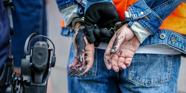 Mensch in Handschellen neben einem Polizisten