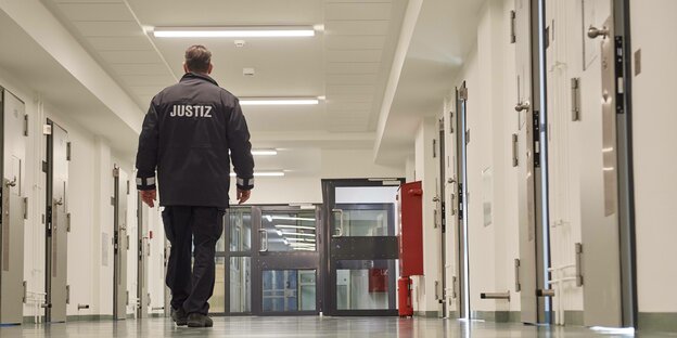 Ein Justizvollzugsbeamter geht einen Flur mit Zellentüren entlang.