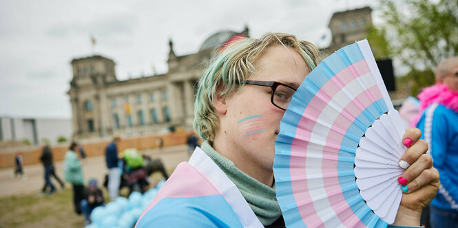 Protest vor dem Reichstag, eine Person verdeckt die Hälfte seines Gesichts mit einem bunten Fächer