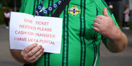 Ein Fan hält ein Schild hoch, auf dem auf Englisch steht: "Ein Ticket benötigt, Bargeld oder Überweisung, ich habe das Uefa Portal"