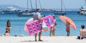 Ein Tourist mit einer rosafarbenen Luftmatratze in Form eines Handys an einem Strand auf Mallorca