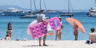 Ein Tourist mit einer rosafarbenen Luftmatratze in Form eines Handys an einem Strand auf Mallorca