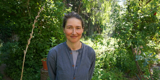 Eine Frau schaut in die Kamera, hinter ihr ist der Permakulturgarten zu sehen