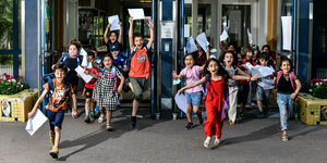 Schüler*innen rennen mit ihren Zeugnissen in der Hand aus einem Schulgebäude heraus