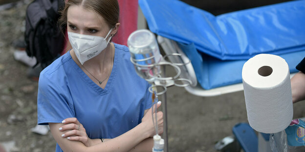 A woman wearing a face mask stands in the rubble of a bombed clinic