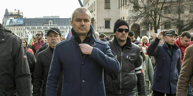 Kostadin Kostadinov bei einem Protestmarsch in Sofia, Bulgarien umringt von Männern, die genauso grimmig schauen wie er - in Hintergrund eine russische Flagge