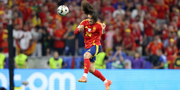 Ein Fußballer mit langen lockigen Haaren in rotem Trikot köpft einen Fußball