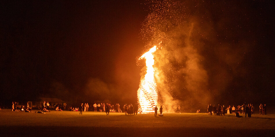 Ein Kreis an Menschen steht in Strahwalde am 22. Juni 2024 um ein etwa zehn Meter großes Holzfeuer