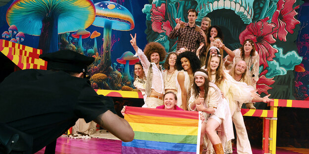 Schauspieler und Schauspielrinnen posieren mit einer Regenbogenfahne auf einer Bühne