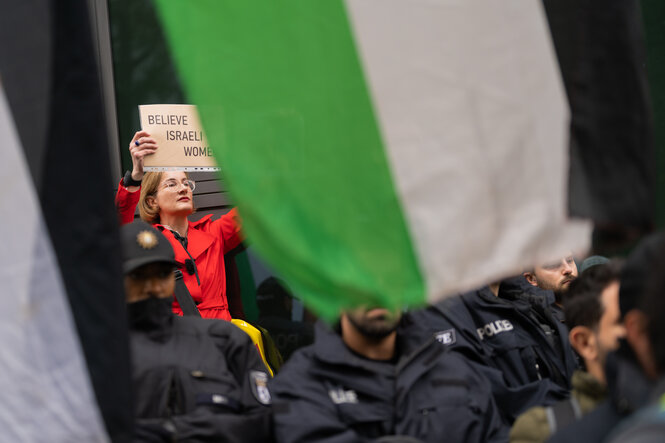 Karolin Preisler in rot hinter Polizisten und einer palästinensischen Flagge