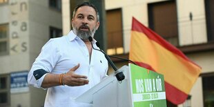 Santiago Abascalvon der Partei VOX hält eine Rede, er steht an einem Rednerpult mit Mikrophon, hinter ihm weht eine spanische Flagge