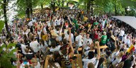 Aufsicht auf einen Biergarten, wo viele Leute in Deutschlandtrikots stehen, im Hintergrund eine Leinwand mit Fußball