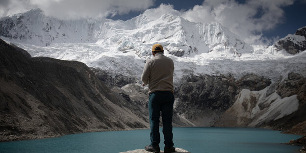 Eine Person steht vor einer Gebirgswand und guckt auf einen Gletschersee
