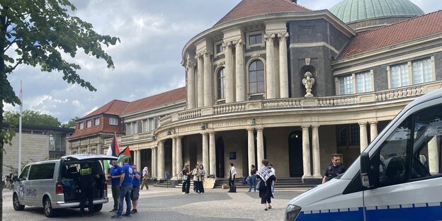 Vor dem Hauptgebäude der Uni Hamburg stehen Polizist:innen und Menschen mit Palästina-Flaggen