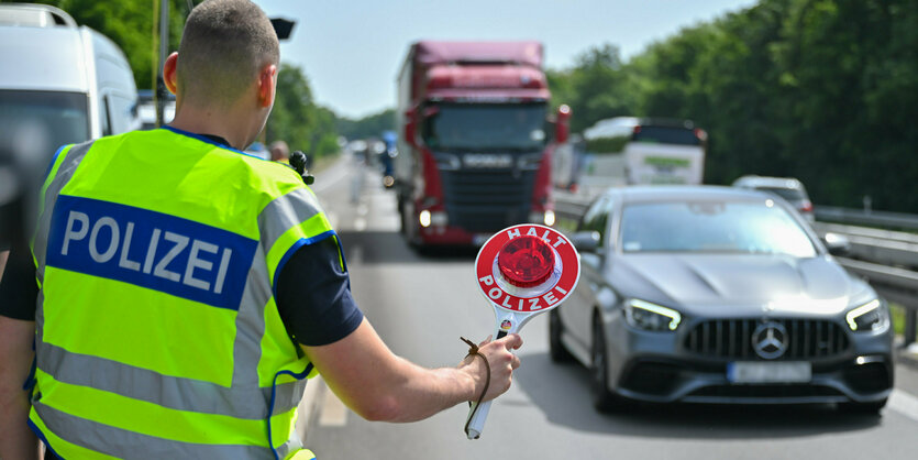 Ein Polizist hält bei einer Grenzkontrolle ein Auto an