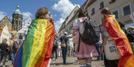 Teilnehmer*innen des Christopher Street Days versammeln sich mit Regenbogenfahnen auf dem Marktplatz in Prina