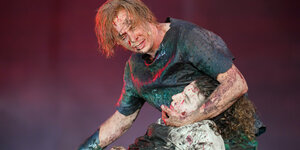 Schauspieler Franz Pätzhold spielt Dietrich von Bern, er hat Blut im Gesicht und greift um den Kopf eines Nebendarstellers