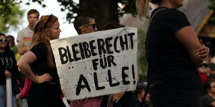 Demonstranten stehen mit Banner Bleiberecht für Alle! auf einer Wiese am Dorint Hotel, dem Tagungsort der Innenministerkonferenz, während einer Demonstration gegen Abschiebungen anlässlich der Innenministerkonferenz (IMK) in Potsdam, 20. Juni 2024.