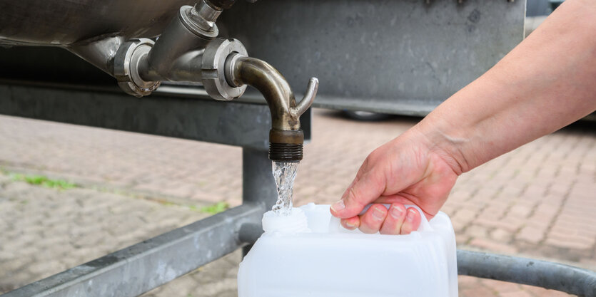 An einer Entnahmestelle wird mit einem Kanister Wasser geschöpft