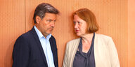 Robert Habeck und Lisa Paus stehen an einer Holzwand im Kabinett und sprechen miteinander
