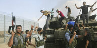 Bewaffnete Kämpfer stehen vor einem Panzer auf dem junge Männer stehen