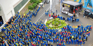 viele Menschen in blauen Anzügen mit gelben Helmen stehen vor einer Bühne