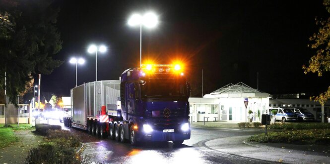 Nachtstimmung ein Lastwagen mit großen gelben Scheinwerfern an der Fahrerkabine fährt mit Behältern beladen auf einer nassen Straße