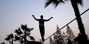 Ein Mann balanciert auf einer Slackline, nur seine Silhouette ist zu erkennen.