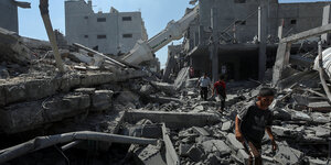 Menschen laufen auf den Ruinen zerstörter Häuser, im Hintergrund ein umgestürztes Minarett