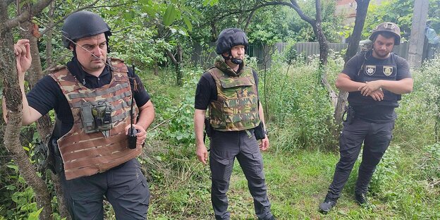 Drei Polizisten mit schußsicheren westen und Helmen stehen in einem Garten unter Bäumen