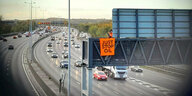 Großaufnahme einer Londoner Autobahn, die von der Aktivistengruppe "Just Stop Oil" blockiert wird. Zu sehen ist einer der Aktivisten beim anbringen eines Banners auf einer Stauanzeige hoch über der befahrenen Autobahn.