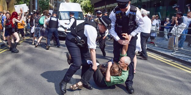 Ein Demonstrant wird von zwei britischen Polizisten von der Straße getragen