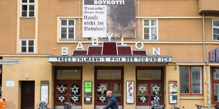 Eine Hausfassade, an der ein Plakat hängt, im Fenster sind Davidsterne zu sehen