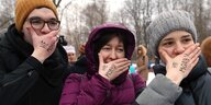 Drei Frauen hölten ihre Hände vor ihre Münder, auf den handrücken stehen Worte in kyrillischen Buchstaben