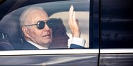 Joe Biden sitzt in einem Auto und winkt