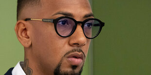 Portrait von Jérôme Boateng. Er hat ein weißes Hemd und ein dunkles Jackett an. Er trägt eine Brille mit rundem, dunklen, großen Rahmen. Boateng hat einen Bart, der seinen Mund umfasst bis zum Kinn runter. Ansonsten glattrasiert.