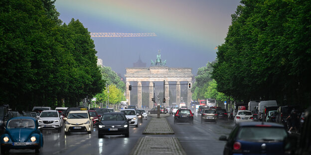 Während des Regens ist für einen kurzen Moment ein Regenbogen über dem Brandenburger Tor und der Straße des 17. Juni zu sehen.