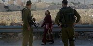 eine junge palästinensische Frau schaut auf zwei Soldaten an einem Checkpoint