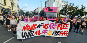 Menschen beim Internationalist Queer Pride Berlin Neukölln am 22. Juli 2023. Auf dem Fronttransparent steht: „None of us are free until all of us are free”.