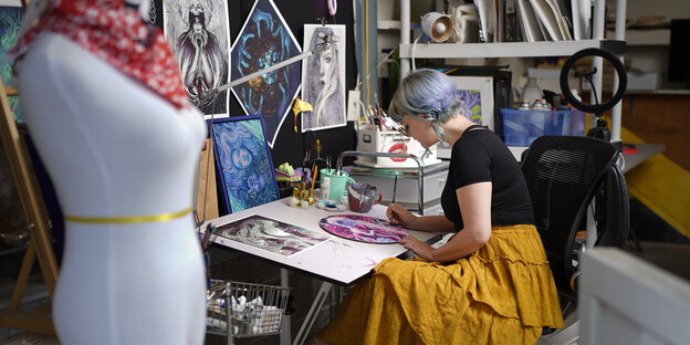Eine Frau sitzt am Zeichentisch in einem Kunstatelier
