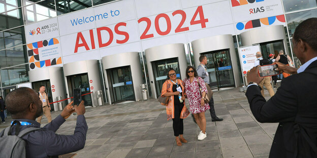 Besucher*innen der 25. Welt-Aids-Konferenz lassen sich auf dem Messegelände vor dem Haupteingang fotografieren