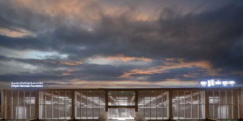 BLick auf ein Lagerhallen-artiges Ausstellungshaus mit dramatischem Himmel