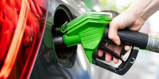 Eine Frau hält an einer Tankstelle an einer Zapfsäule eine Zapfpistole in der Hand und betankt ein Auto