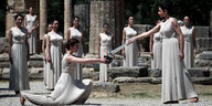 Frauen in vermeintlich antiken griechischen weißen Kleidern zünden eine Fackel an