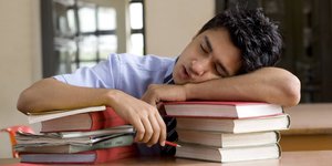 Ein Student schläft auf einem Stapel Bücher