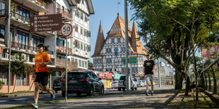 Zwei Jogger laufen auf einer Straße in Blumenau. Im Hintergrund sieht man große Häuser im Fachwerkhaus-Stil