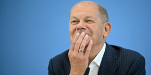 Bundeskanzler Olaf Scholz hat das Kinn auf seine Hand gestützt und lächelt