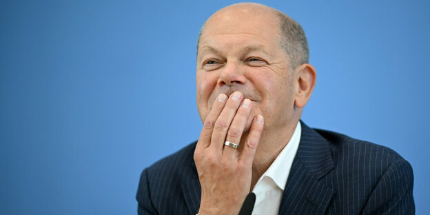 Bundeskanzler Olaf Scholz hat das Kinn auf seine Hand gestützt und lächelt