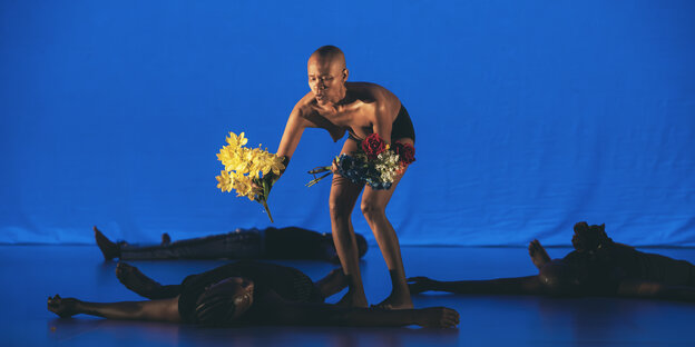 Eine Tänzerin legt vorsichtig Blumen auf am Boden liegende Körper ab
