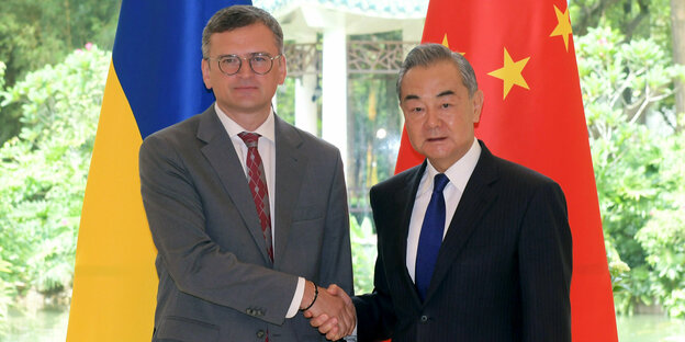 Ukrainischer und chinesischer Außenminister vor zwei Flaggen, händeschüttelnd
